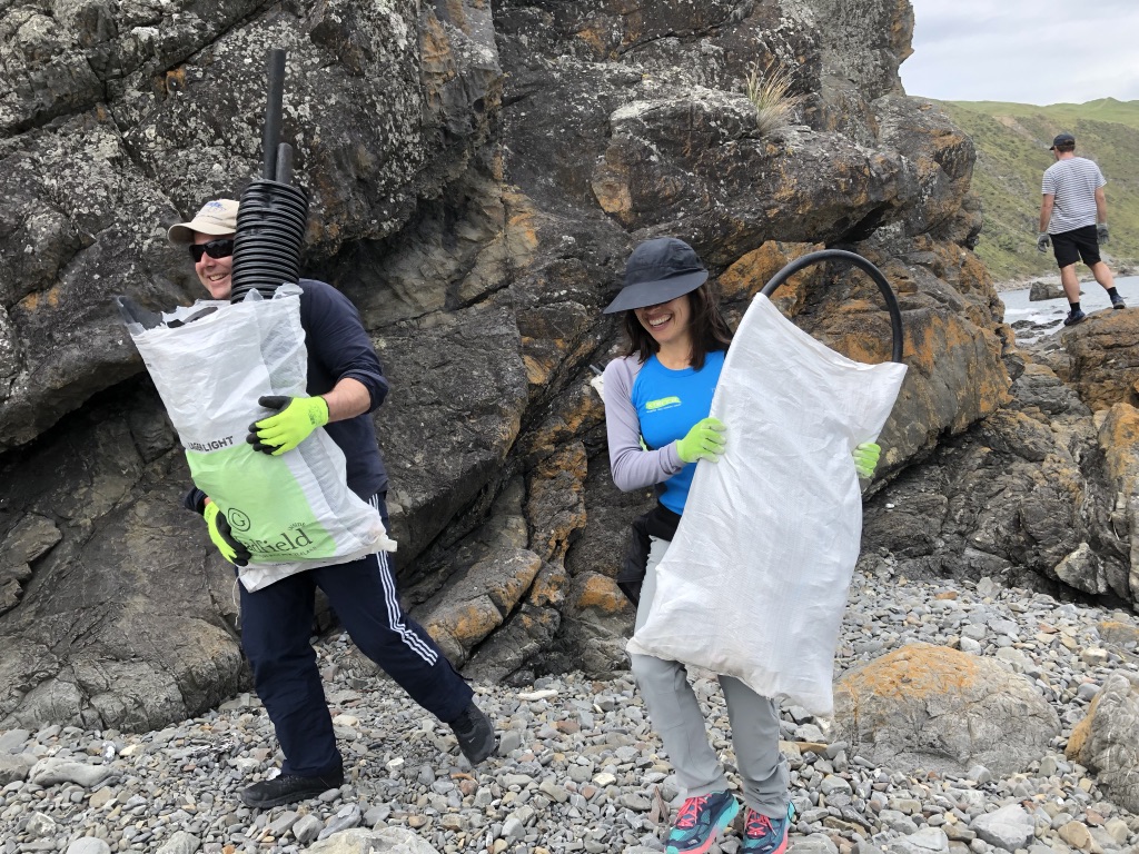 Photo of two people carrying bags of rubbish by some rocks